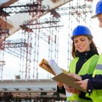 Teamwork-in-construction-industry---two-engineers-working-together-on-construction-site-with-blueprints-and-plans-645373486